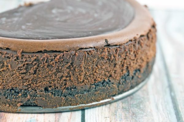 side view of a dark chocolate cheesecake showing the oreo crust, chocolate cheesecake, and chocolate ganache topping