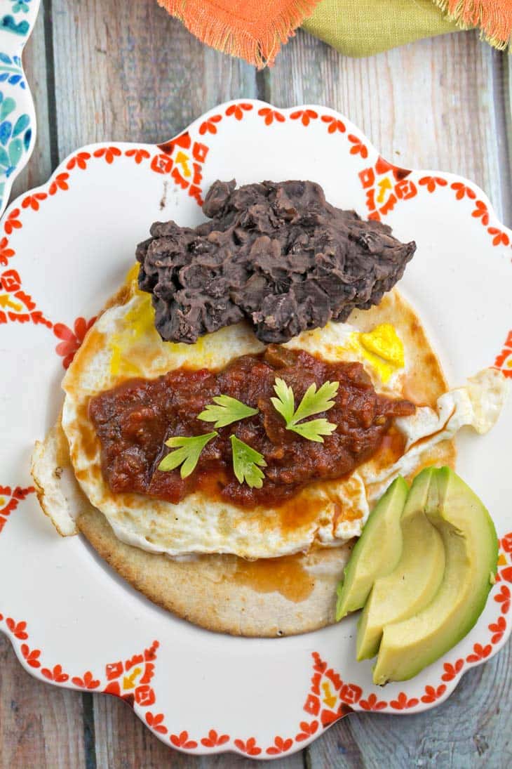 plate with a fried corn tortilla, runny egg, mashed black beans, salsa, and avocado slices.