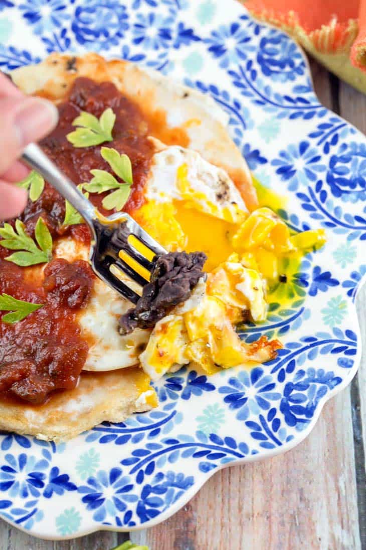 fork dipping black beans and tortilla into runny egg yolks.