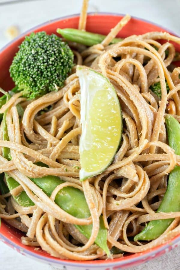 a large bowl of thai peanut noodle stir fry topped with broccoli, snow peas, and sugar snap peas