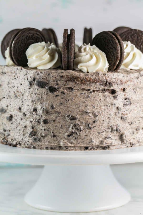 a two layer chocolate oreo cake with oreo cream cheese frosting decorated with whipped cream and whole oreos