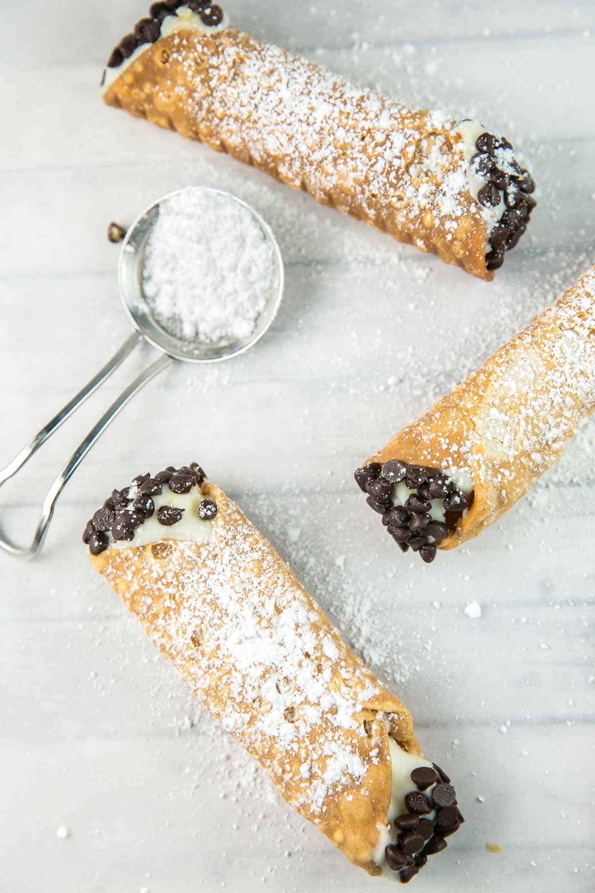 three filled cannolis with a powdered sugar spoon