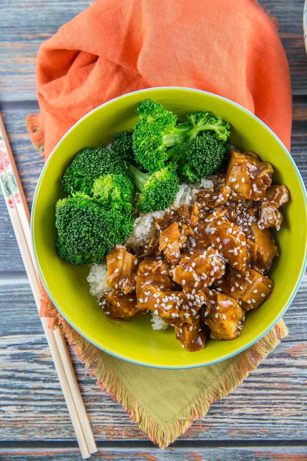 a green bowl filled with sesame honey chicken, bright green broccoli, and rice