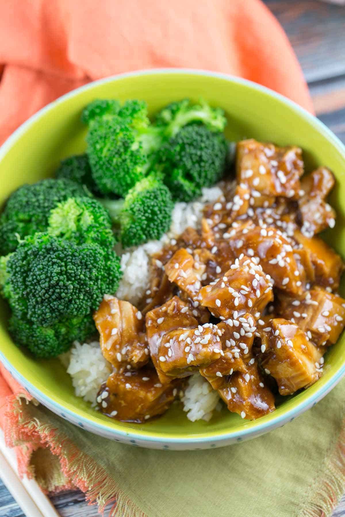 a green bowl filled with cubes of chicken in a honey sesame sauce and steamed broccoli