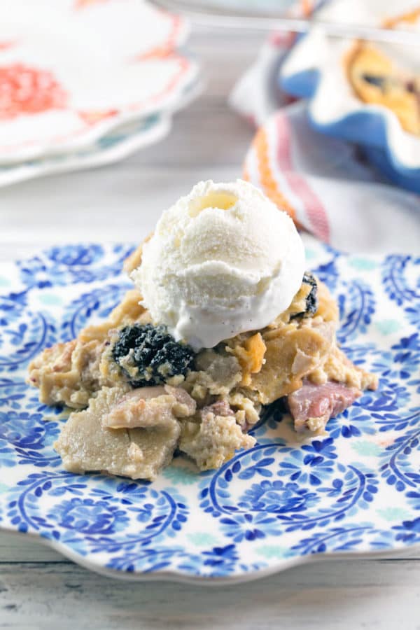 berry clafoutis on a blue plate with a scoop of vanilla ice cream on top