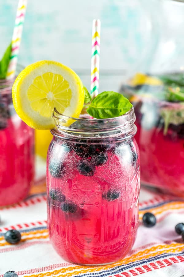 vibrantly pink blueberry basil lemonade with a splash of bourbon in a mason jar with a circle of lemon on the rim