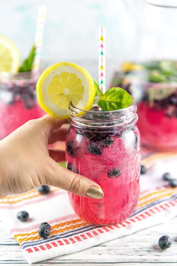 a hand holding a mason jar filled with vibrantly pink naturally colored blueberry basil lemonade