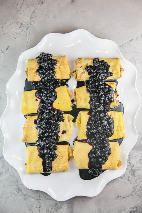 white serving plate with ricotta blintzes covered in homemade blueberry sauce