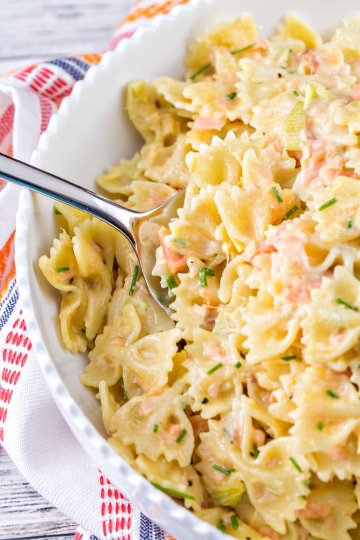 a white serving bowl with a silver serving spoon scooping up thick creamy pasta.