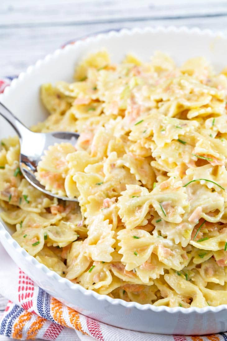 spoon scooping up farfalle pasta with smoked salmon and chopped chives.