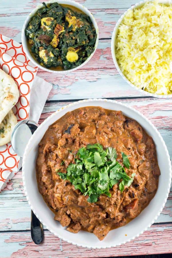 overhead view of an indian dinner with bowls of chicken tikka masala, saag panner, homemade naan, and basmati rice