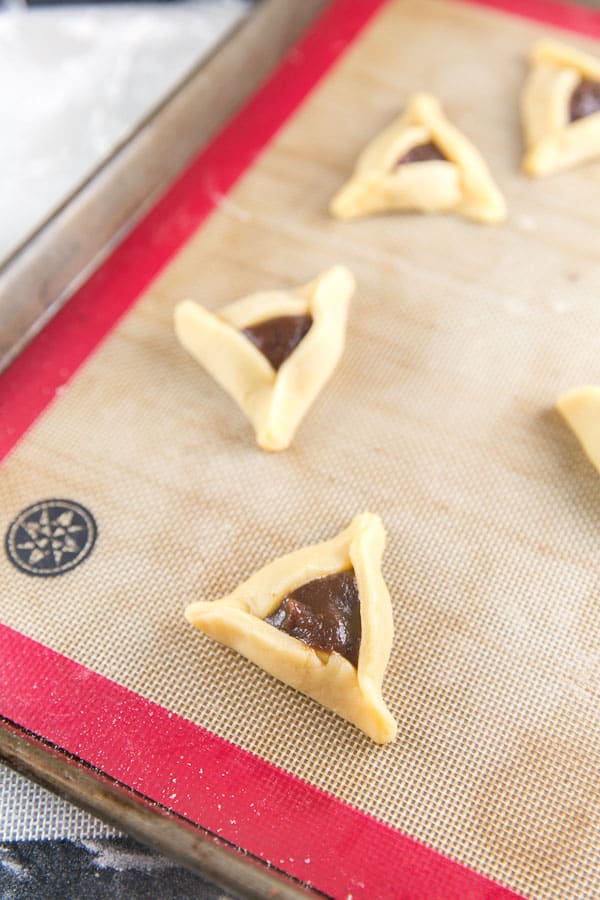 unbaked hamantaschen on a cookie sheet filled with prune filling