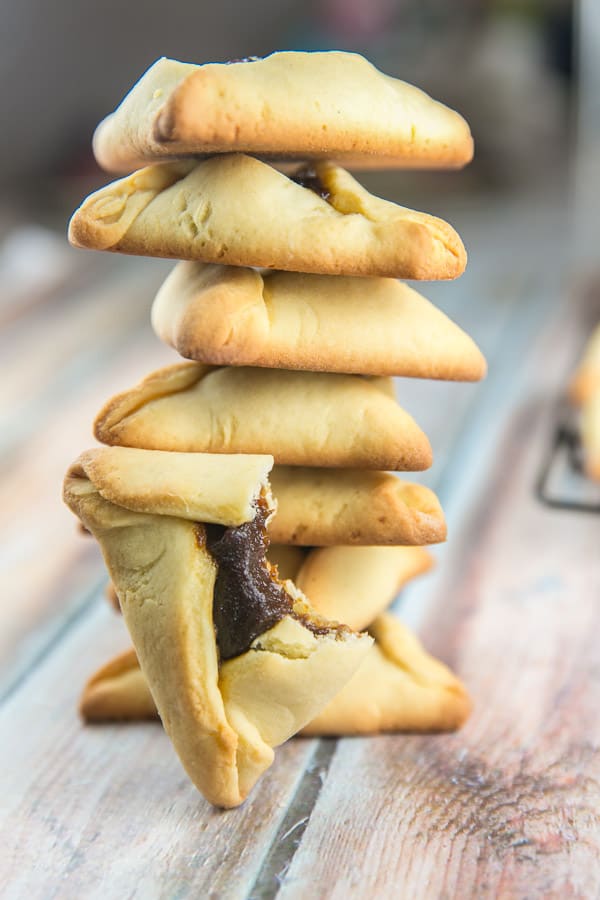 a stack of hamantaschen with one half-eaten hamantasch with a bite taken out of it