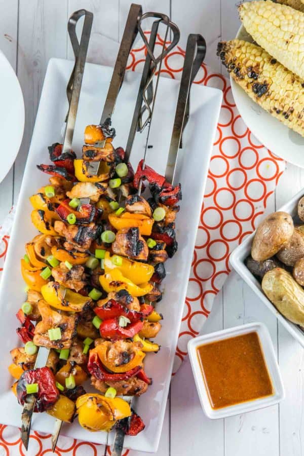 grilled chicken skewers next to grilled potatoes and corn
