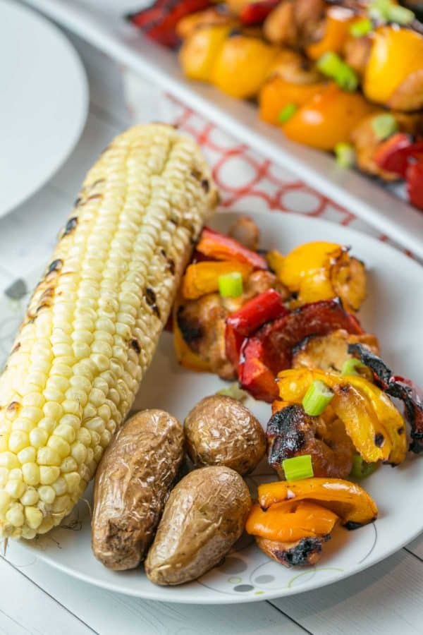 grilled chicken and vegetables on a plate with potatoes and corn