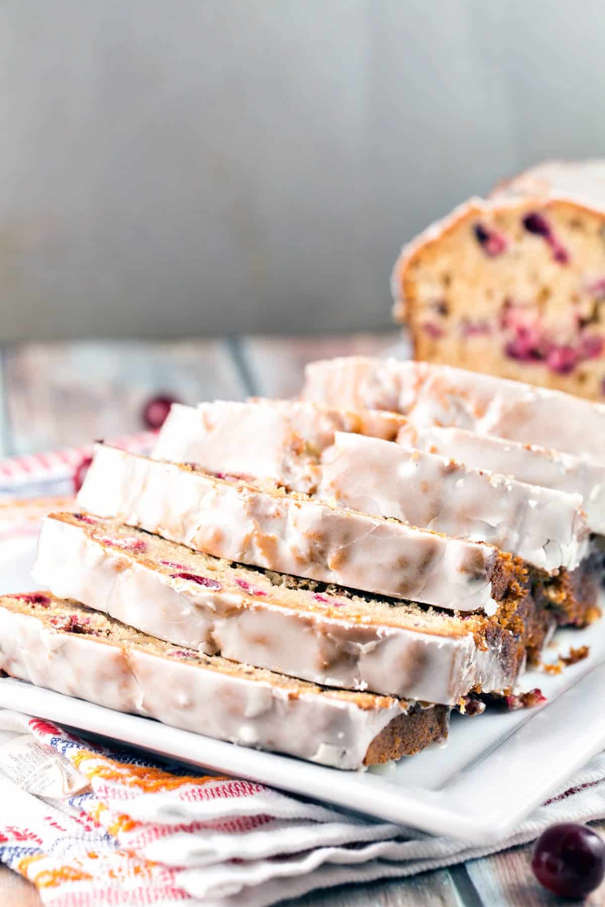 stacked slices of cranberry cider quick bread on a white plate with a gray background