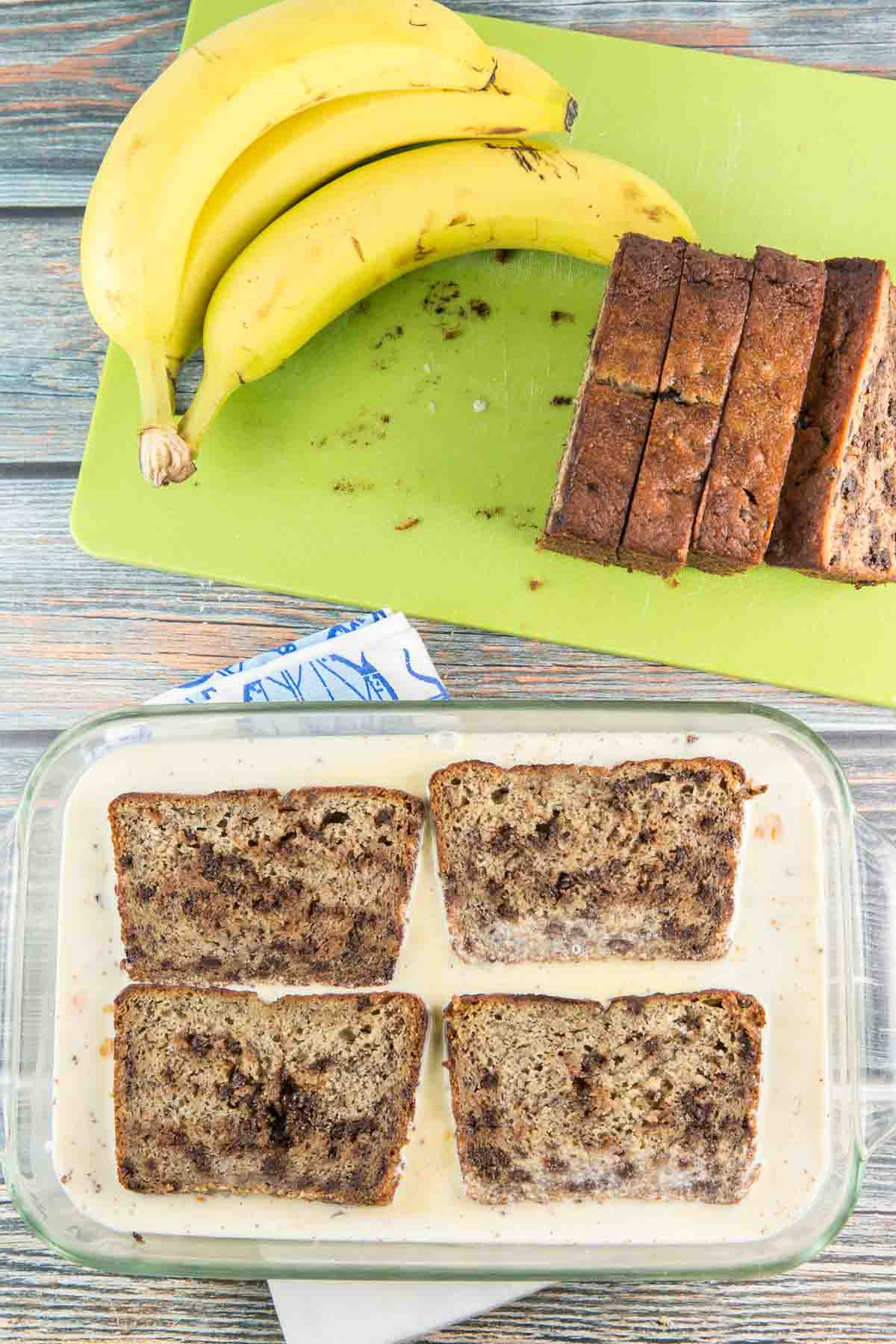 four slices of banana bread soaking up custard in a glass pan