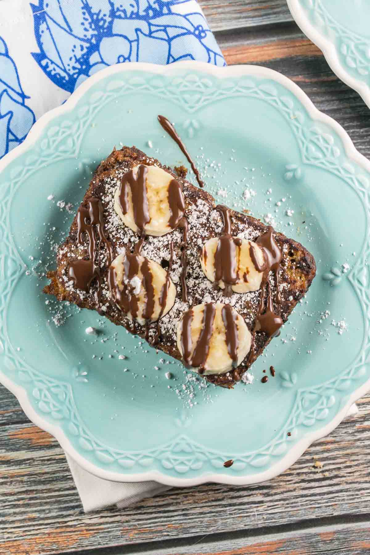 close up view of a slice of french toast covered with chocolate and bananas.