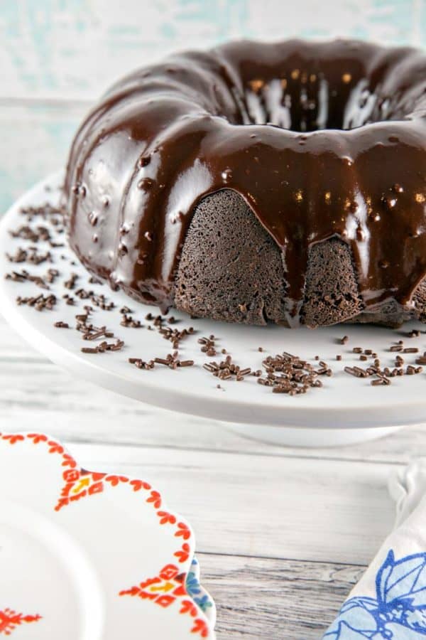 白いケーキプレートの上に光沢のあるチョコレートガナッシュで覆われたチョコレートファッジバントケーキの側面図チョコレート振りかける