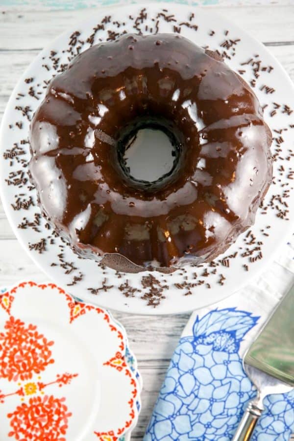 overhead photo of a chocolate fudge bundt cake covered in soft shiny chocolate ganache on a white serving plate