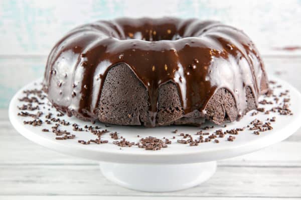 a dark chocolate bundt cake covered in chocolate ganache on a white cake plate