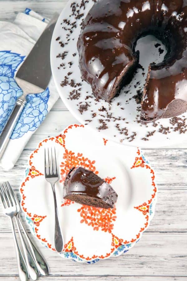 overhead view of a chocolate fudge bundt cake covered in chocolate ganache with one slice missing and placed on an orange floral dessert plate