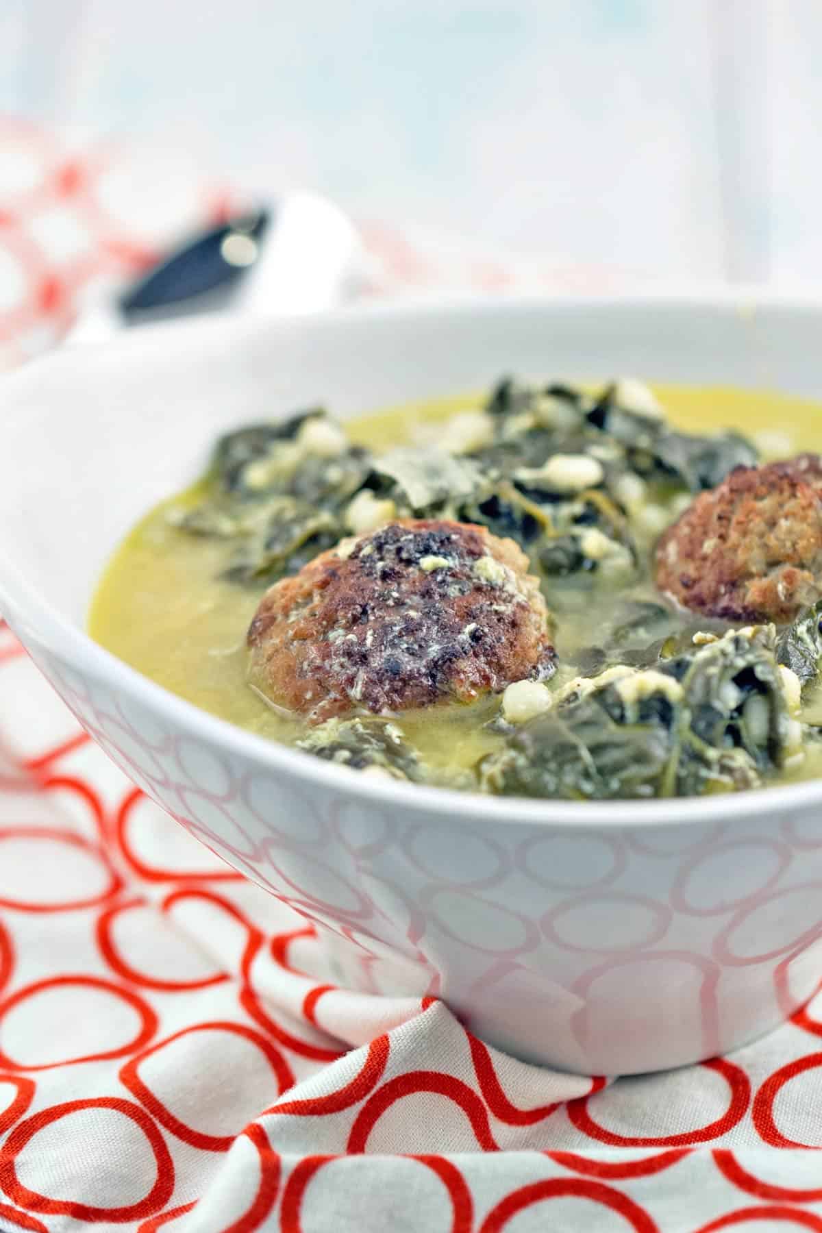 side view of a bowl of italian wedding soup with two meatballs