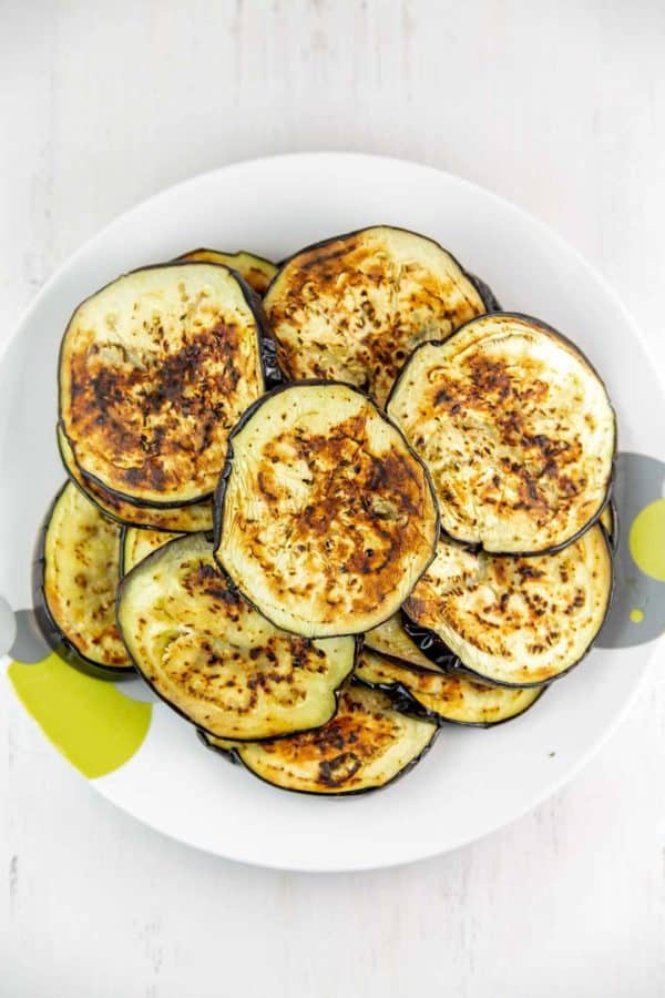 rounds of sauteed eggplant piled up on a plate
