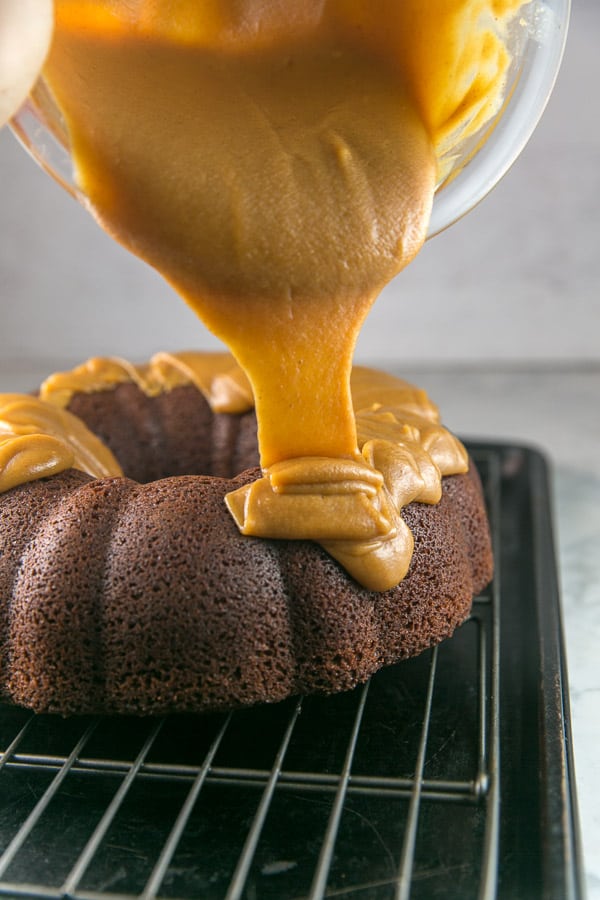 peanut butter ganache flowing from a mixing bowl onto a chocolate bundt cake