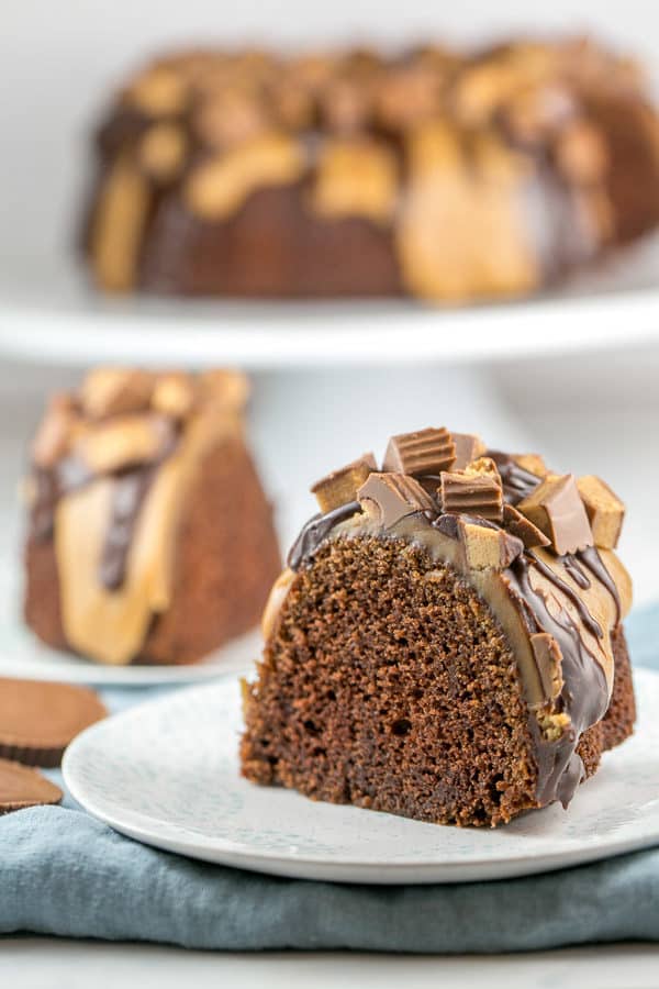 two slices of a chocolate peanut butter cup bundt cake on small dessert plates with the rest of the cake on a cake stand in the background