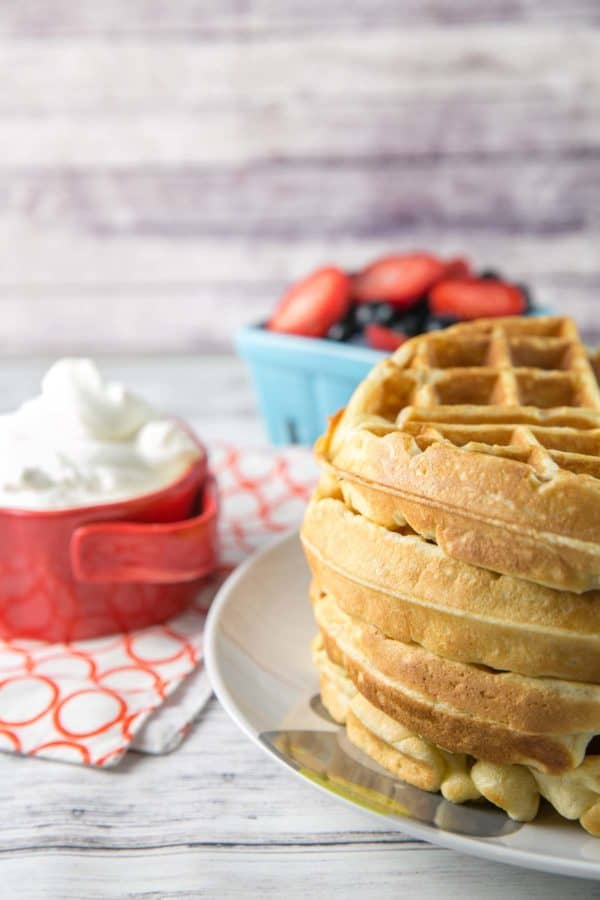 stack of waffles with whipped cream and berries in the background