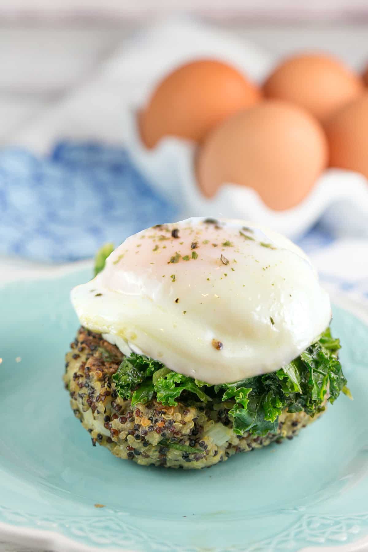 side view of a tricolored quinoa cake covered in kale and a poached egg on a blue plate