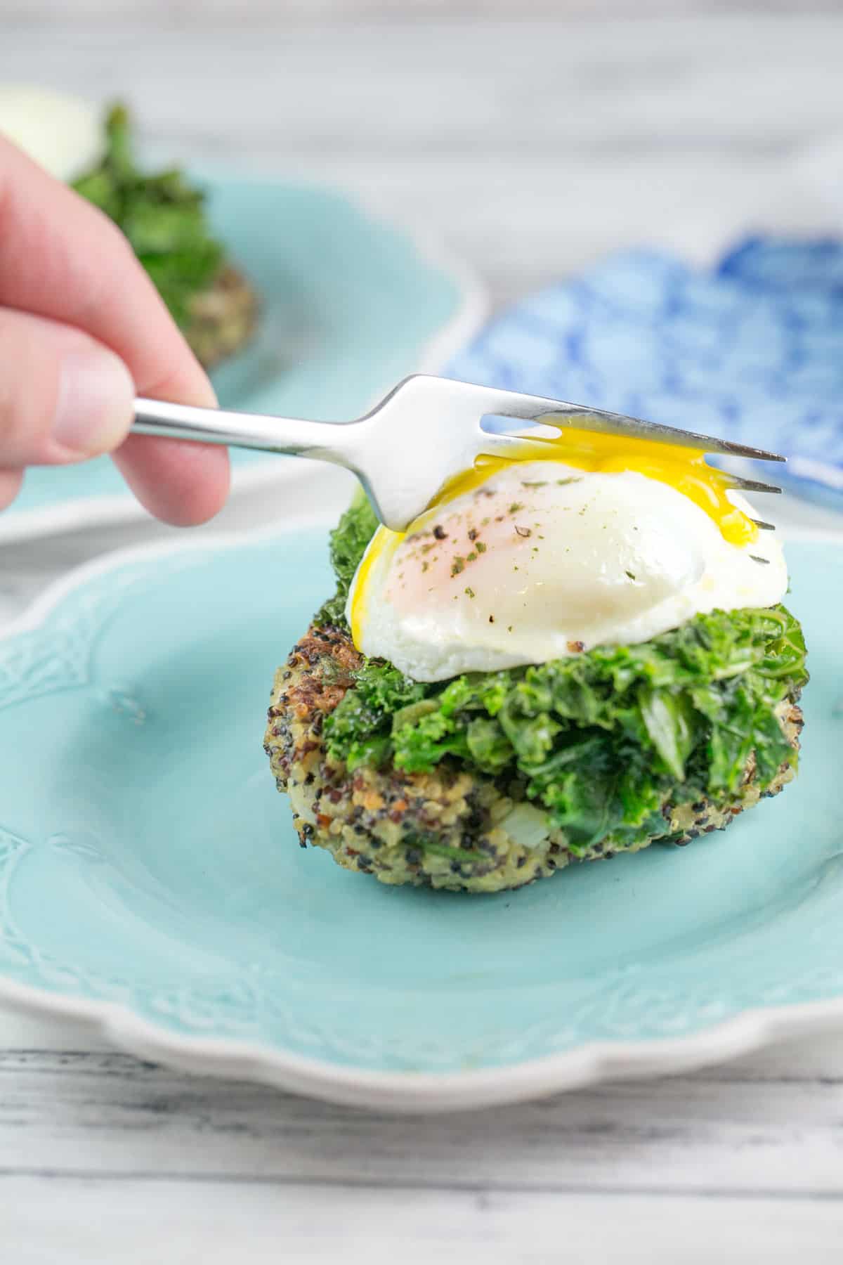 side view of a quinoa cake topped with a poached egg with a fork breaking open the egg