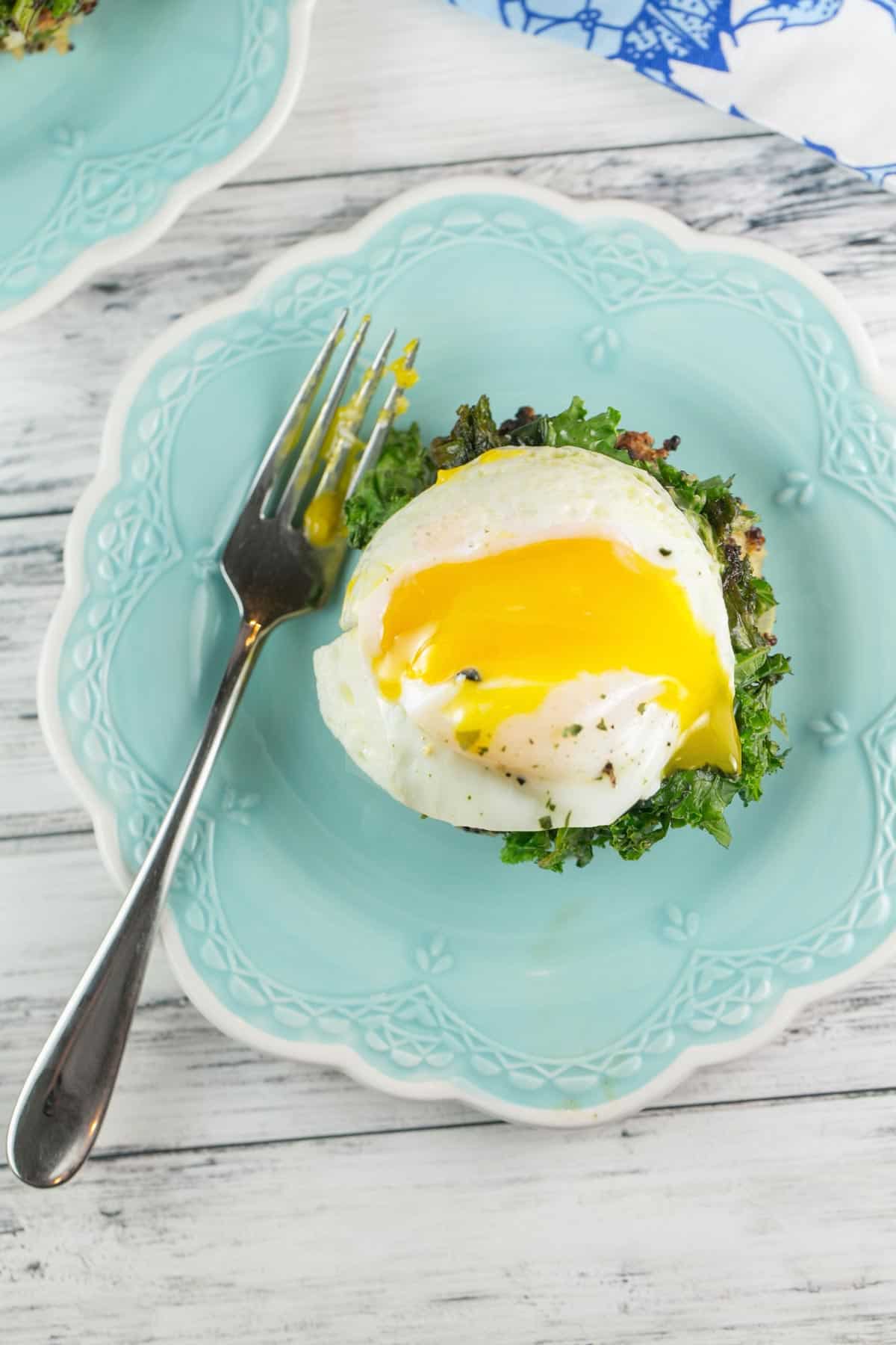 overhead picture of a poached egg with the yolk dripping over kale and a quinoa cake