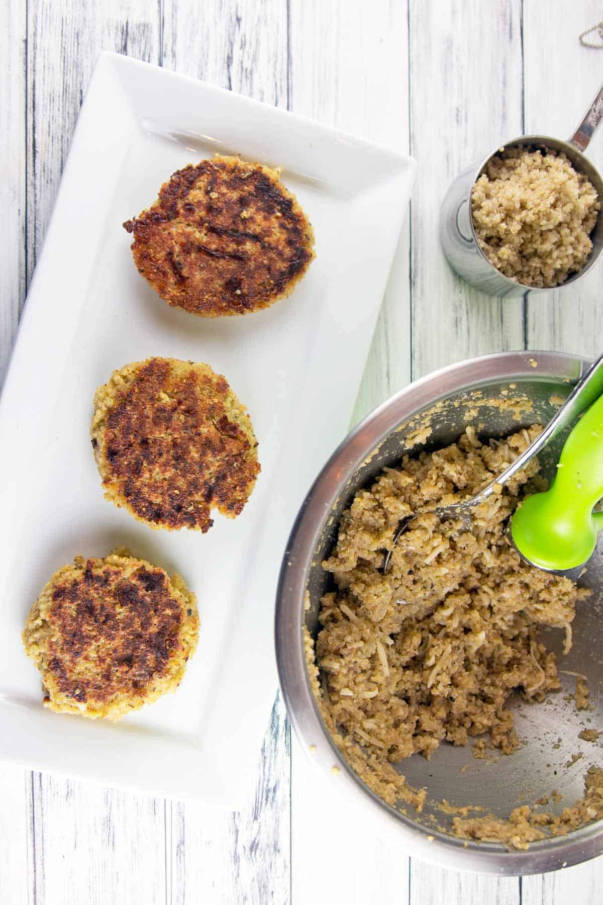 overhead photo of quinoa cakes on a white rectangular plate with a mixing bowl with the quinoa cake mixture