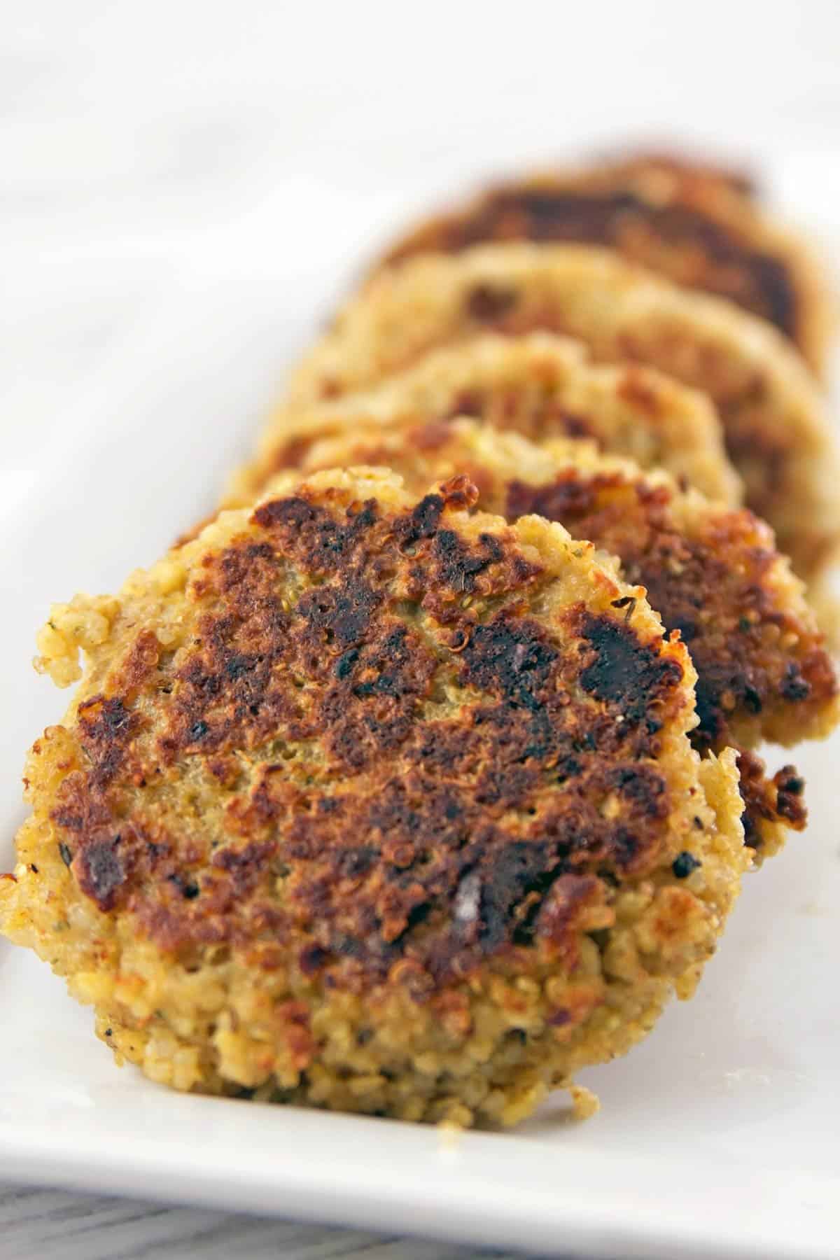 cooked quinoa cakes stacked on a white rectangular serving plate