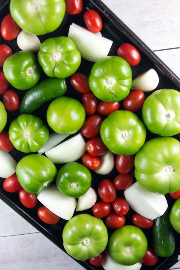 a sheet pan with fresh tomatillos, cherry tomatoes, onions, and peppers which will turn into salsa verde