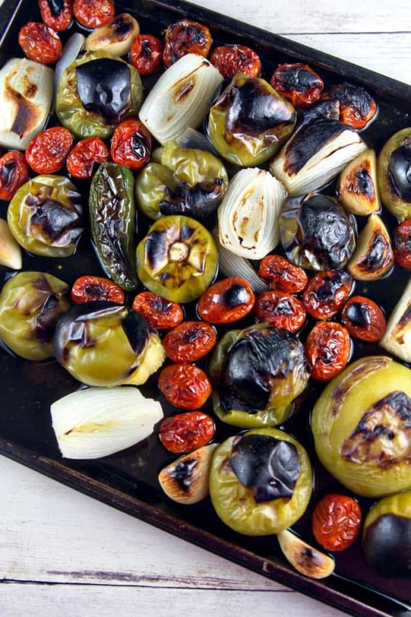 a sheet pan filled with roasted and charred tomatillos, cherry tomatoes, onions, and jalapenos