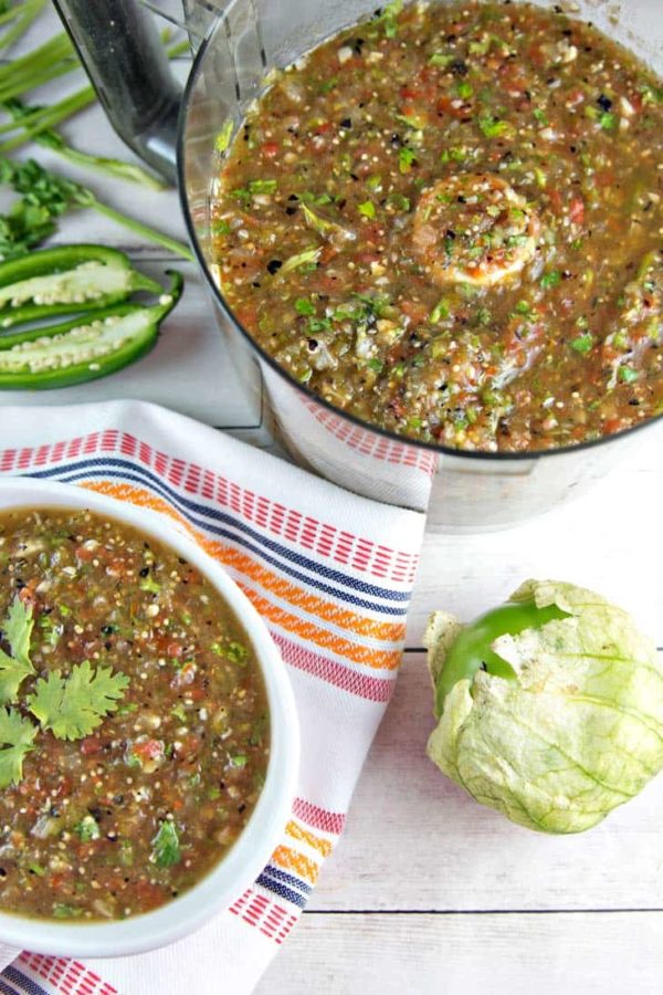 homemade roasted tomatillo salsa verde in a food processor next to a whole tomatillo