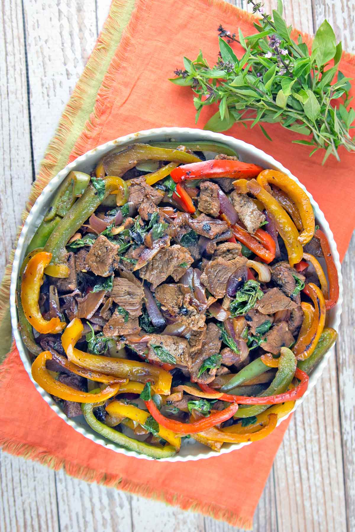 overhead photo of beef, red yellow and green peppers, and thai basil on an orange placemat