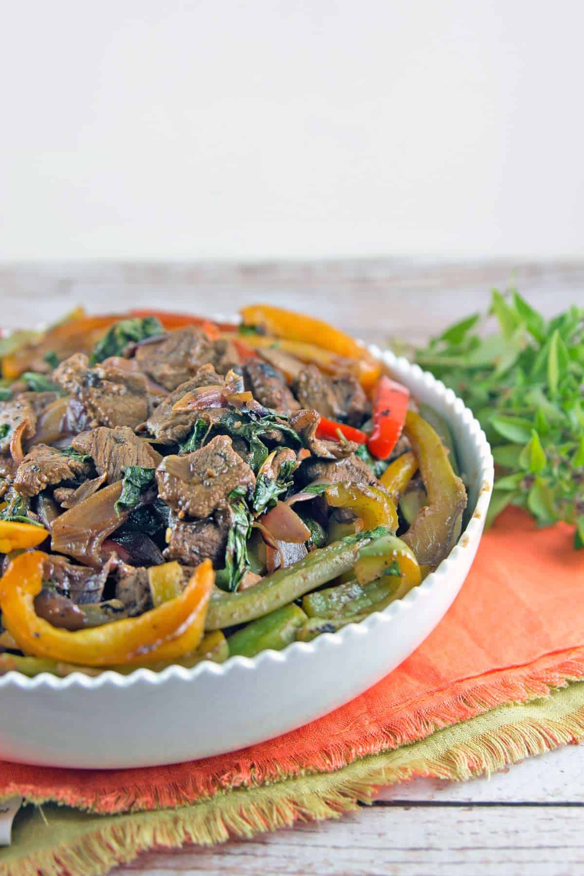 bowl of thai basil beef stir fry with fresh thai basil in the background