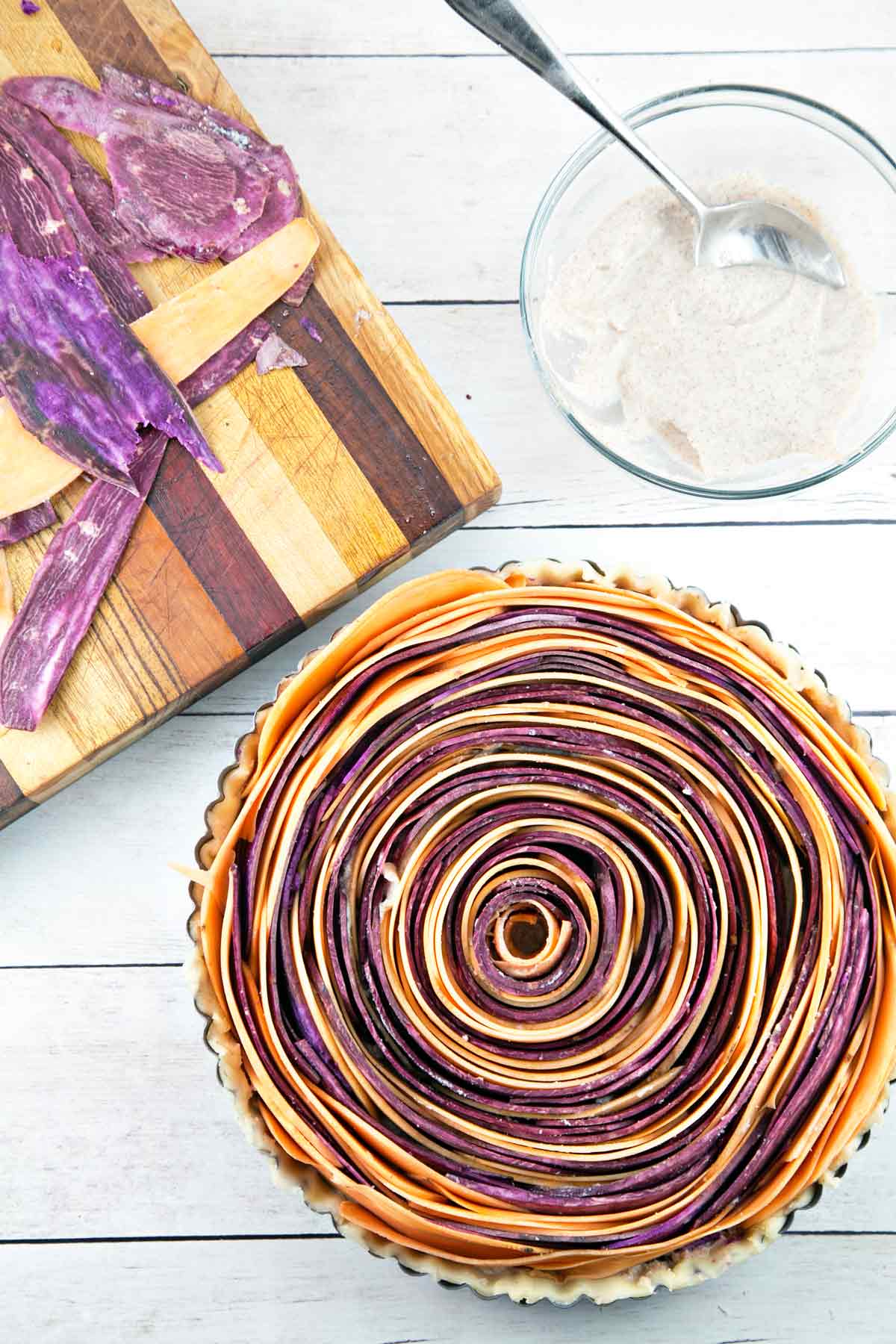 overhead view of unbaked spiral sweet potato tart next to a wooden cutting board.