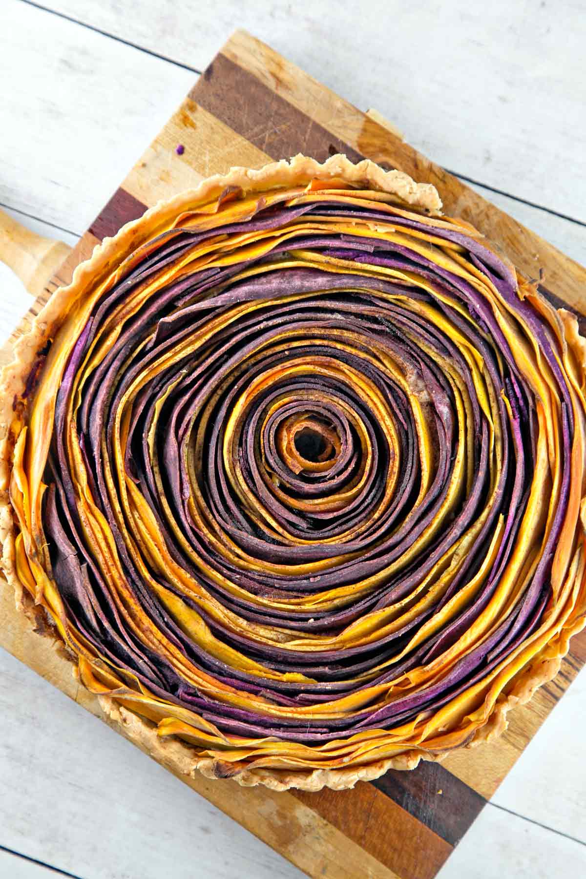 baked sweet potato tart made in a spiral design with circles of orange and purple potatoes.