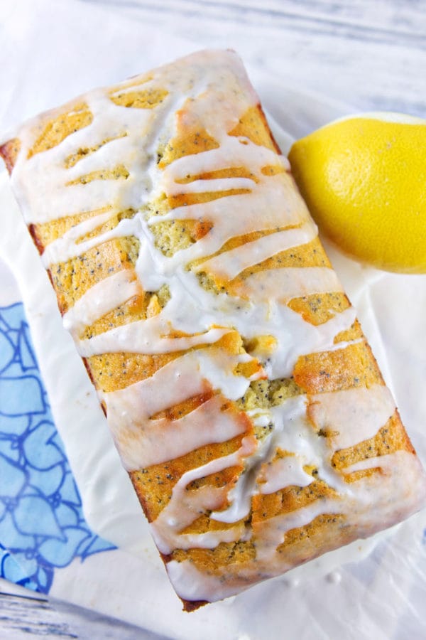 loaf of lemon poppy seed bread covered with lemon glaze next to a whole lemon