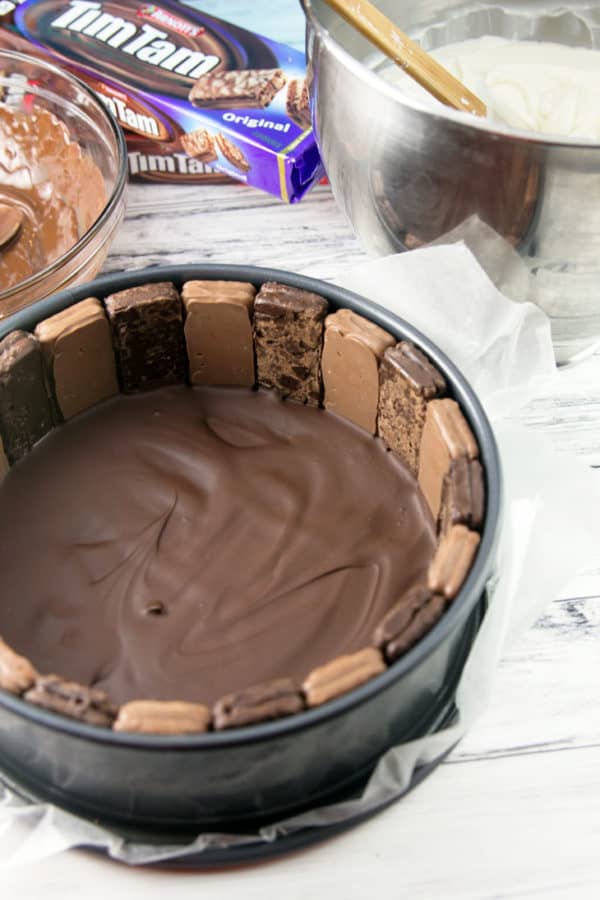 melted chocolate poured in the bottom of a springform pan surrounded by tim tams