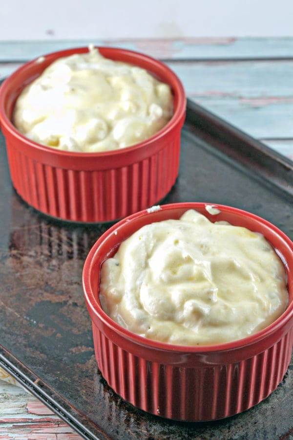 two individual sized ramekins filled with unbaked macaroni and cheese souffle