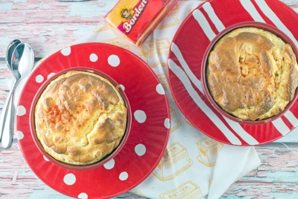 two red ramekins filled with macaroni and cheese souffle sitting on decorative red and white plates
