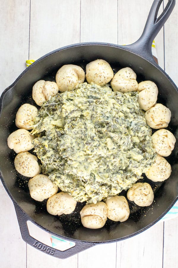 cast iron pan filled with spinach and artichoke dip surrounded by balls of biscuit dough