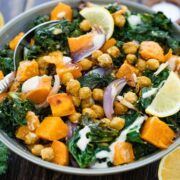 large bowl filled with kale, roasted sweet potatoes, spicy chickpeas, and tahini dressing.