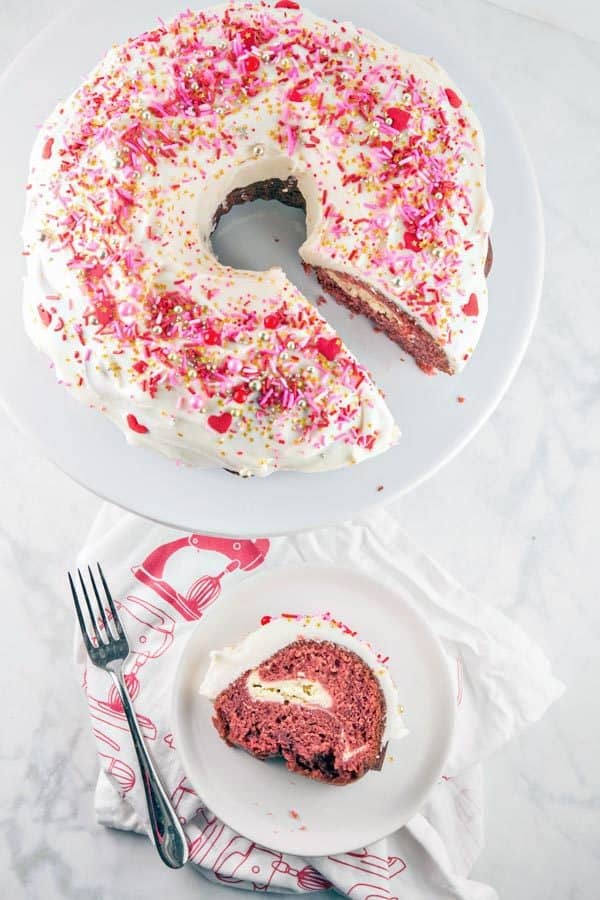 red velvet bundt cake covered with cream cheese frosting with one slice on the side